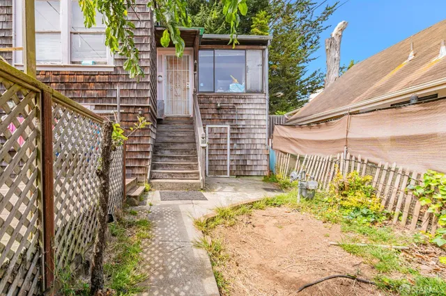 a view of yellow house with a small yard and wooden fence and potted plants