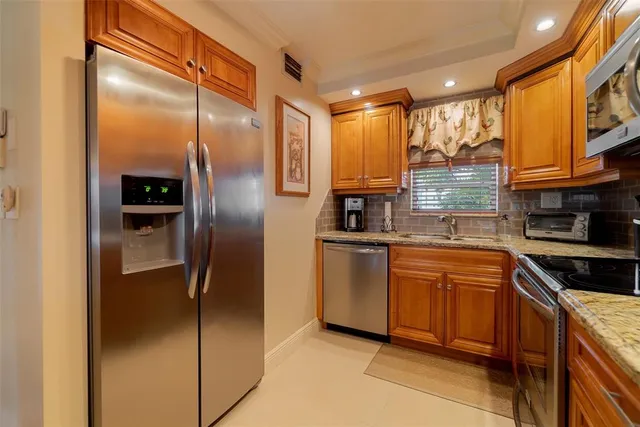a kitchen with stainless steel appliances granite countertop a sink a refrigerator and a wooden cabinets