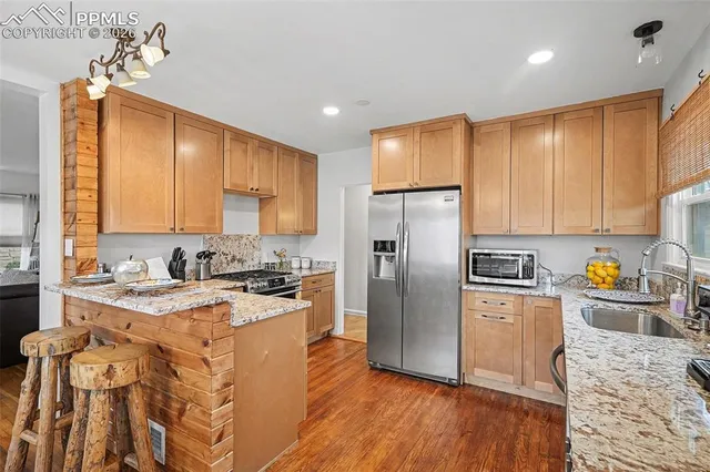 a kitchen with stainless steel appliances granite countertop a refrigerator a sink dishwasher a stove with wooden cabinets and floor