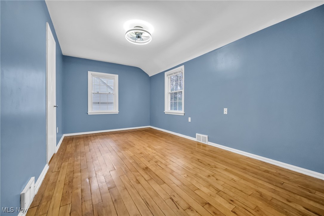 1605 Laclede Road Cleveland, OH 44121 - Photo 23 of 40 Unfurnished room featuring hardwood / wood-style flooring, lofted ceiling, visible vents, and baseboards