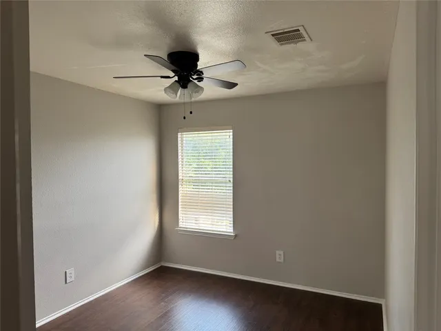 an empty room with wooden floor fan and windows