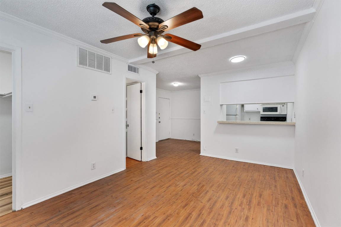Unfurnished living room with crown molding, a textured ceiling, wood finished floors, and a ceiling fan