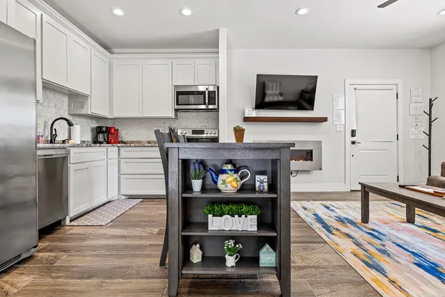 a open kitchen with stainless steel appliances granite countertop a stove top oven a sink dishwasher and white cabinets with wooden floor