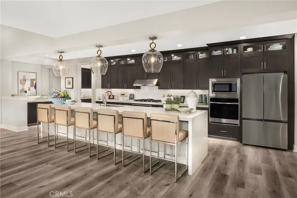 a kitchen with stainless steel appliances kitchen island granite countertop a refrigerator a stove a sink and white cabinets with wooden floor