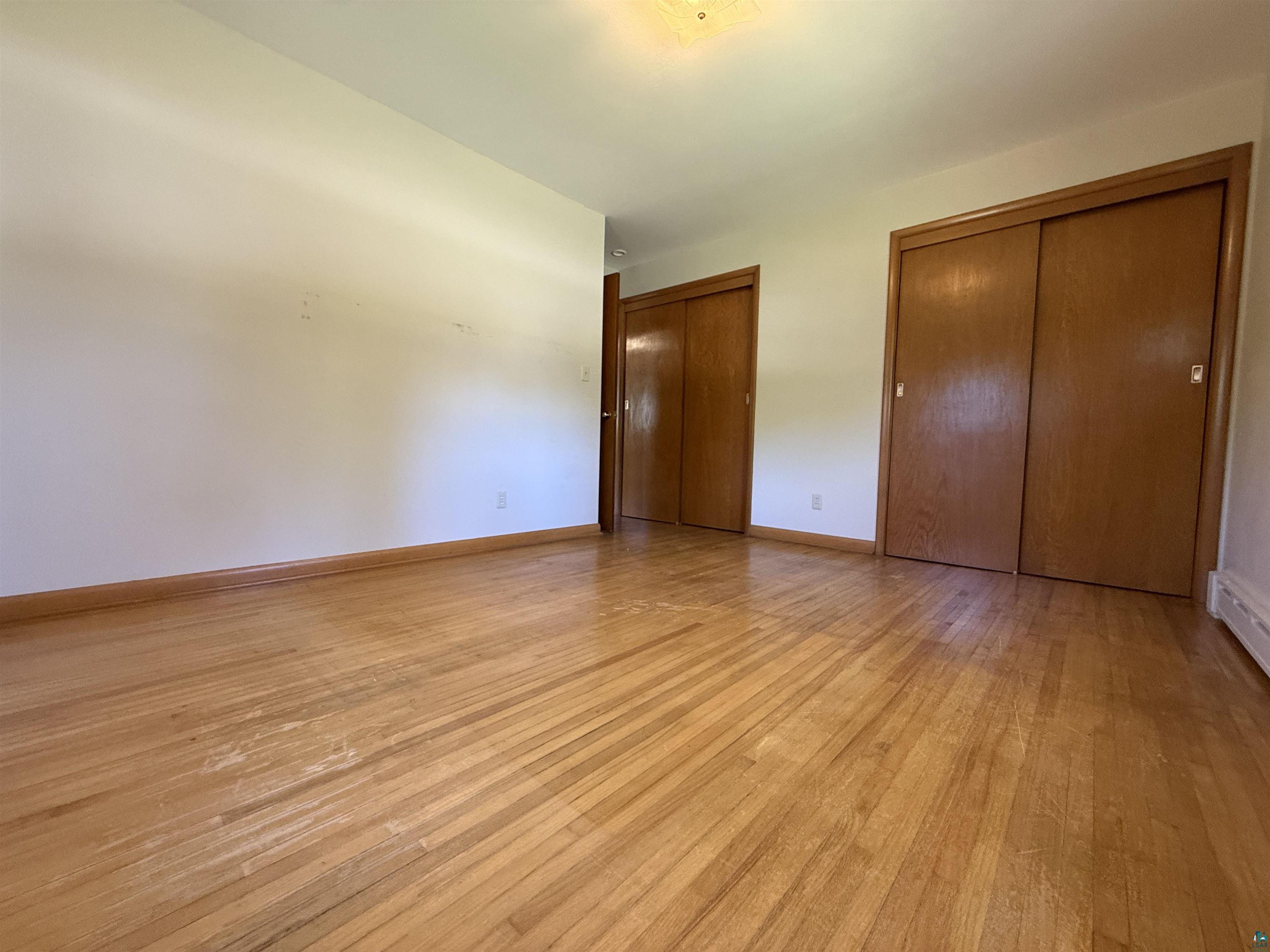607 3rd Street Northeast Chisholm, MN 55719 - Photo 14 of 32 Hardwood flooring throughout, featuring two sets of sliding wood-panel closet doors and white baseboards