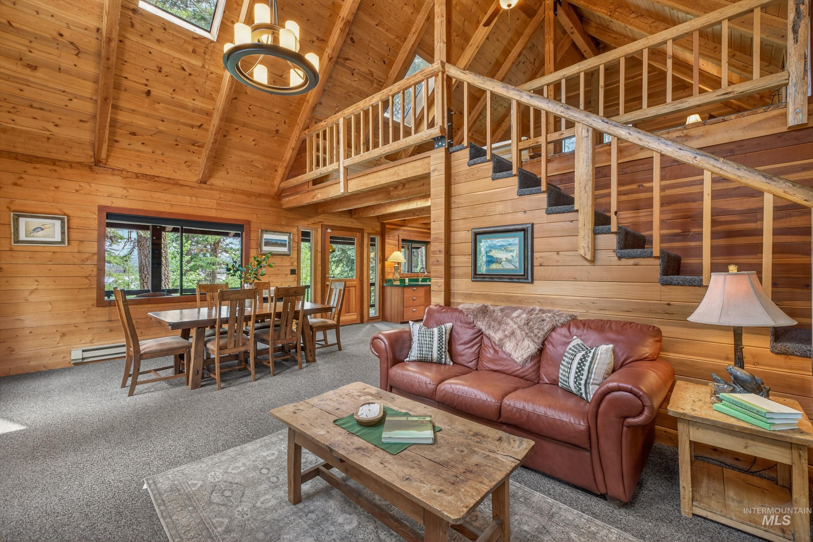 2339 West Mountain Road Donnelly, ID 83615 - Photo 5 of 37 Open-concept interior featuring extensive wood paneling, a vaulted wood-finish ceiling, and a prominent wooden staircase with a matching railing
