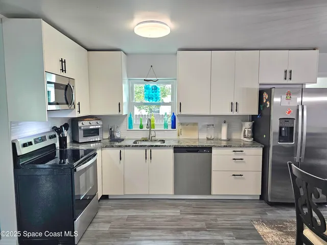 a kitchen with stainless steel appliances granite countertop a stove a sink dishwasher a refrigerator and white cabinets with wooden floor