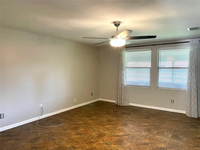 an empty room with a chandelier fan and windows