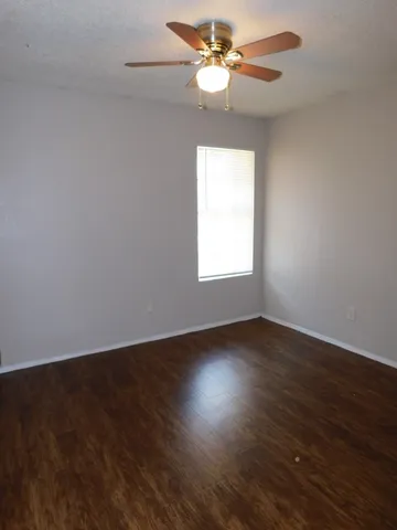 an empty room with wooden floor fan and windows
