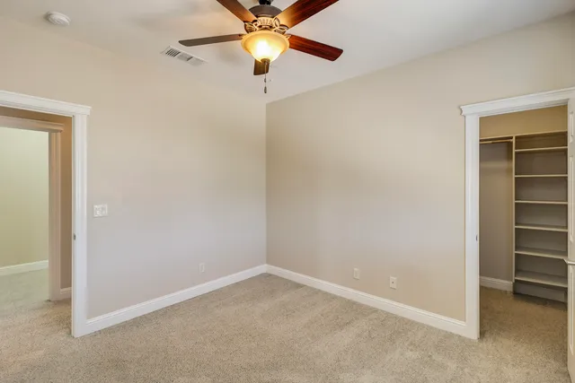 an empty room with ceiling fan and windows