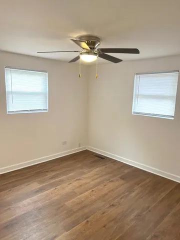 a view of an empty room with wooden floor and a ceiling fan
