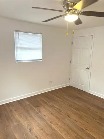 a view of an empty room with wooden floor and a chandelier fan