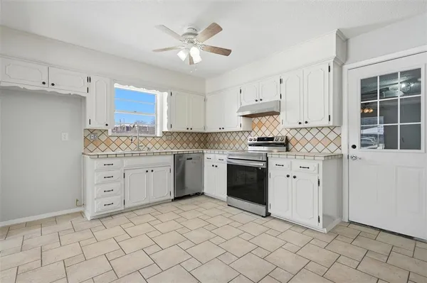 a kitchen with granite countertop white cabinets stainless steel appliances a sink and a window
