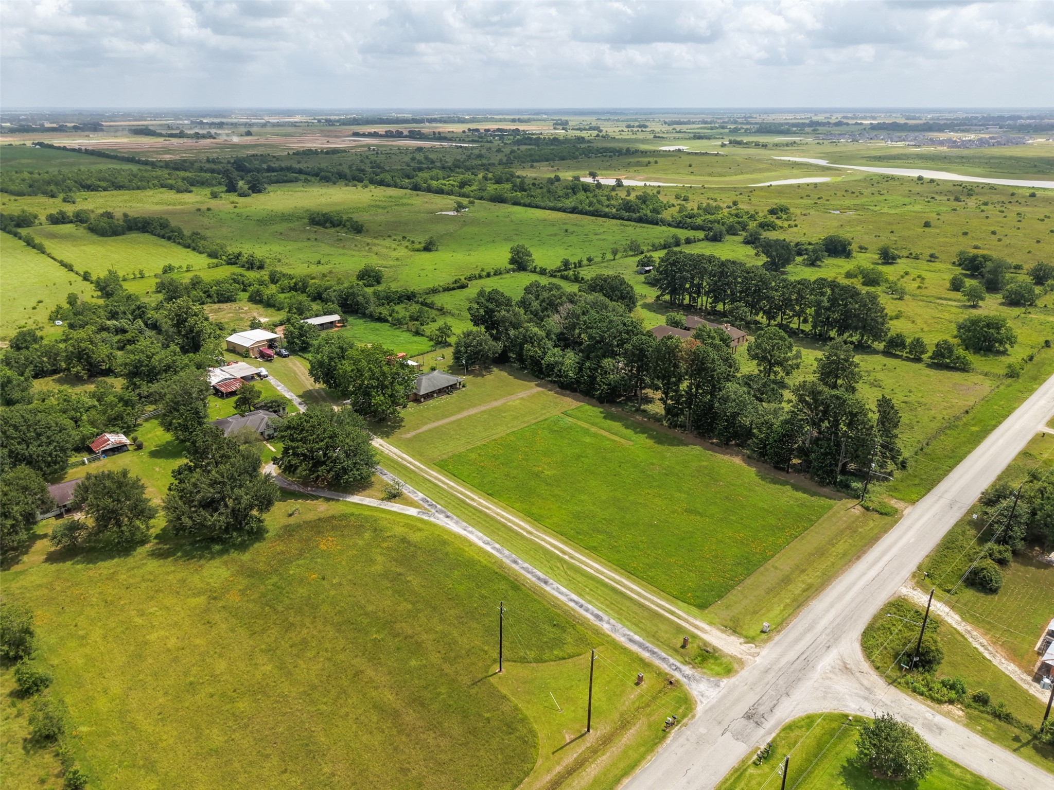 34366 Owens Road Hempstead, TX 77445 - Photo 25 of 46 Wide aerial view showcasing the property's home, barn, open pasture, mature trees, and prominent corner location with ample road frontage and a scenic rural setting.