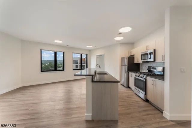 a view of kitchen with stainless steel appliances granite countertop a stove top oven a sink dishwasher a refrigerator and a dining table with wooden floor