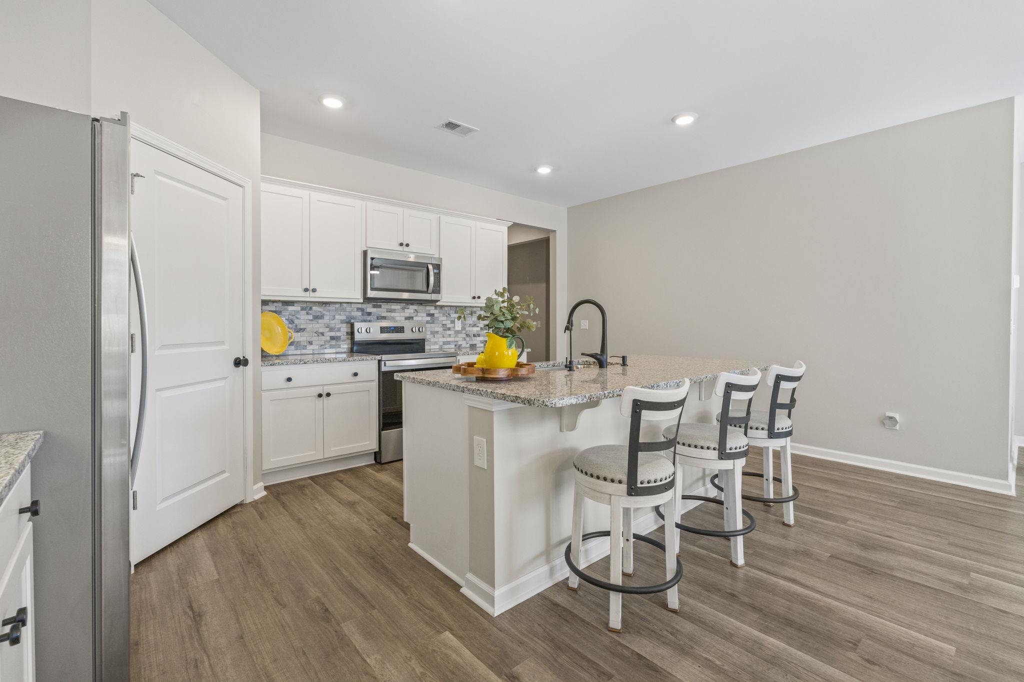 143 Ardeer Court Little River, SC 29566 - Photo 8 of 40 Kitchen with appliances with stainless steel finishes, a kitchen bar, white cabinets, light stone counters, and an island with sink
