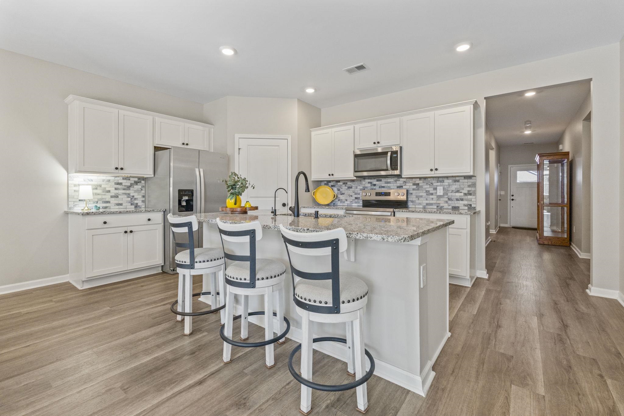 143 Ardeer Court Little River, SC 29566 - Photo 9 of 40 Kitchen with white cabinets, appliances with stainless steel finishes, light stone counters, a kitchen bar, and an island with sink