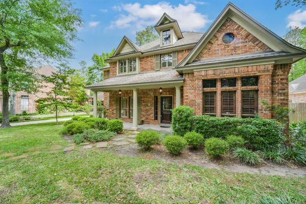a view of a brick house with a small yard plants and large tree