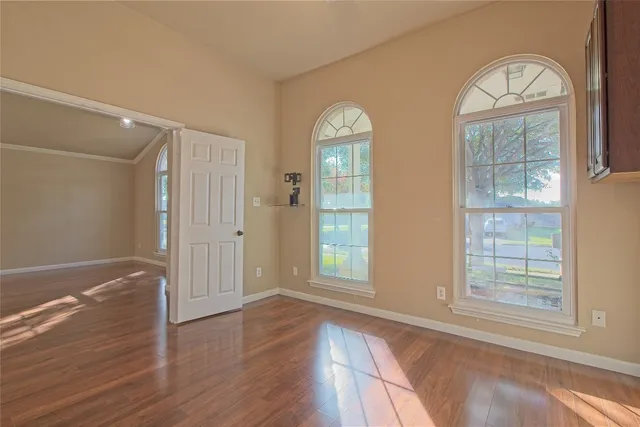 an empty room with wooden floor cabinet and windows
