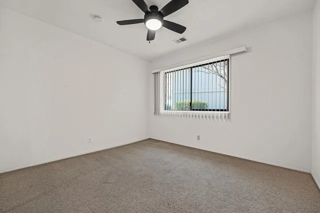 an empty room with ceiling fan and windows