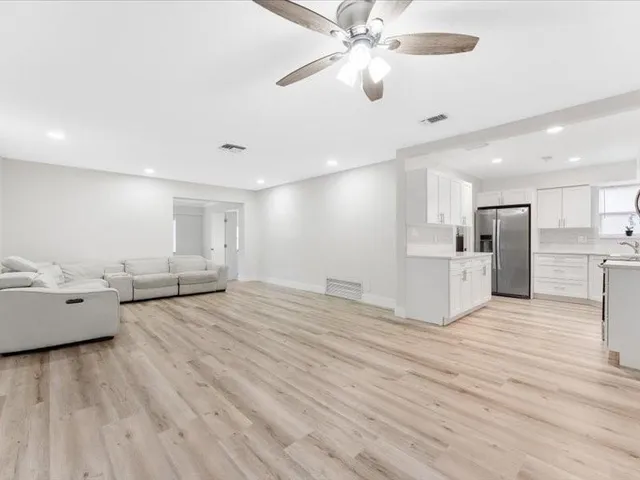 a view of an empty room and kitchen view with wooden floor