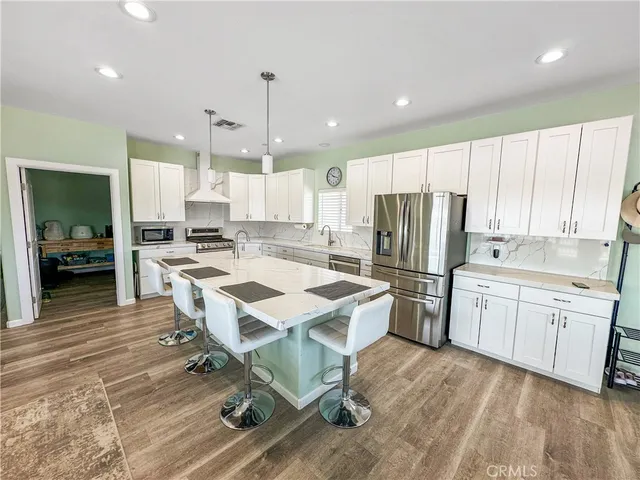 a kitchen with stainless steel appliances kitchen island granite countertop a refrigerator a stove a sink a island and chairs with wooden floor