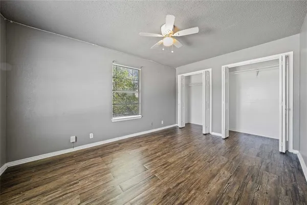 an empty room with wooden floor chandelier fan and windows