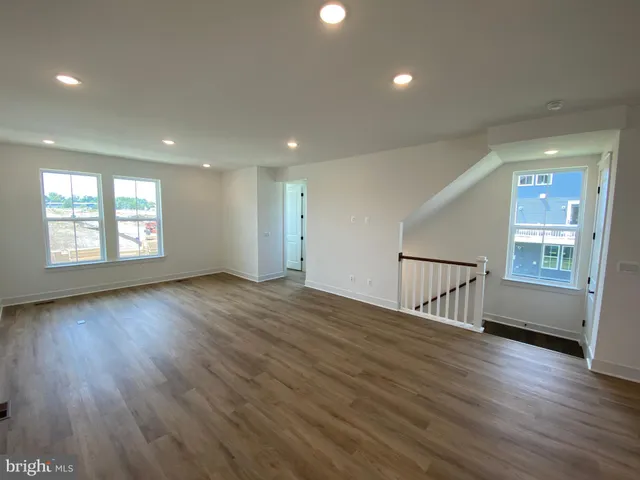 a view of an empty room with wooden floor and a kitchen