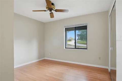 an empty room with wooden floor chandelier fan and windows