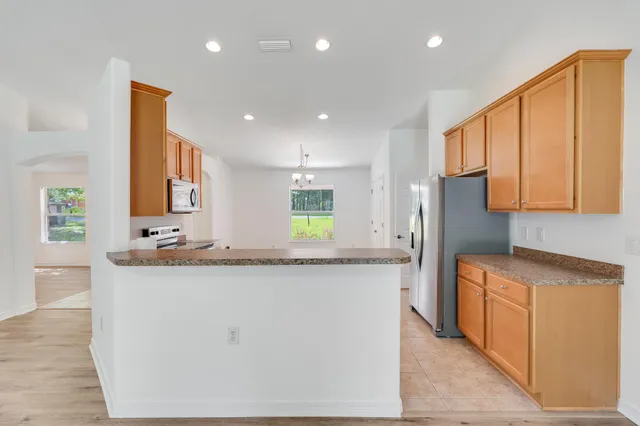 a large white kitchen with a refrigerator a sink dishwasher a stove and a dining table with wooden floor