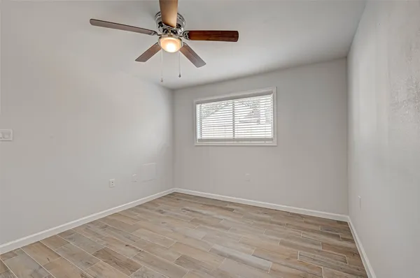 an empty room with wooden floor ceiling fan and window