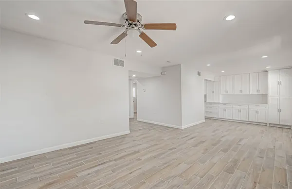 a view of an empty room with wooden floor ceiling fan