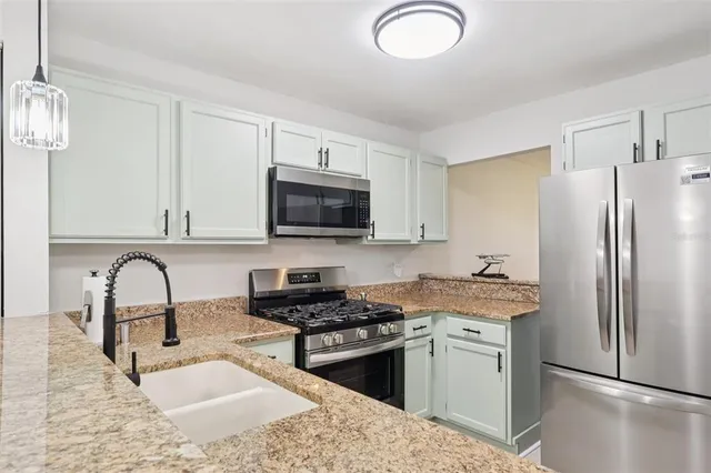 a kitchen with stainless steel appliances granite countertop a sink a stove a refrigerator cabinets and a dining table