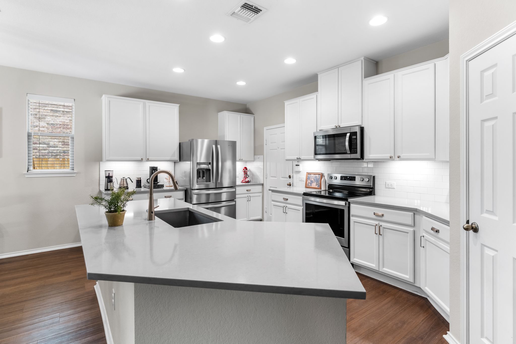 1133 Yellow Iris Road Leander, TX 78641 - Photo 2 of 37 Kitchen featuring an oversized island with an undermount sink, light-toned countertops, white shaker cabinetry, stainless steel appliances, and wood-finish flooring