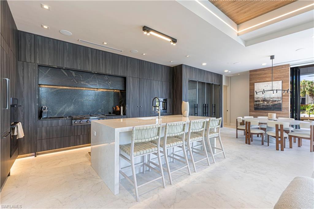 1100 Sandpiper Street Naples, FL 34102 - Photo 45 of 47 Kitchen featuring a marble waterfall island, a built in box effect marble hood area, and cabinets streching across the entire room encasing the custom temperature controlled wine room mirroring the water in the bay