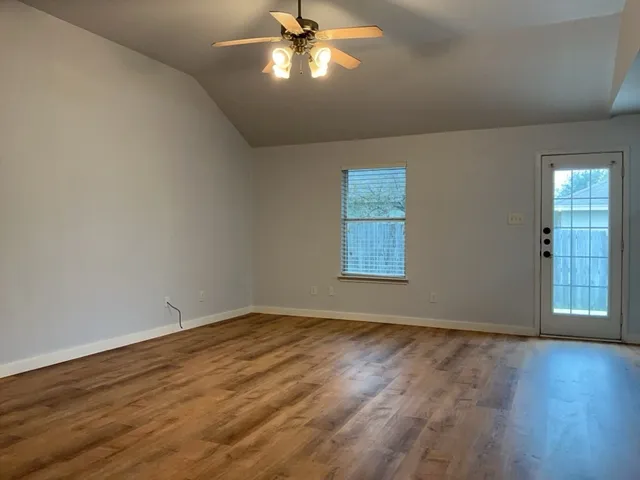 an empty room with wooden floor chandelier fan and windows