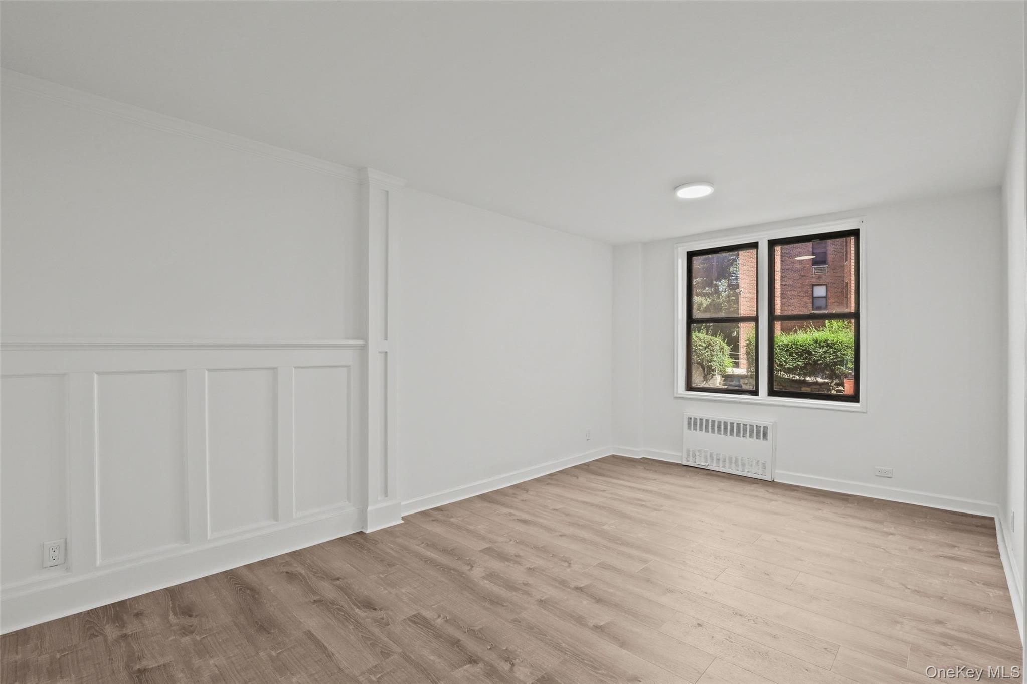 555 Bronx River Road, Unit 1J Yonkers, NY 10704 - Photo 7 of 11 Empty room featuring light wood finished floors, radiator, a decorative wall, and wainscoting
