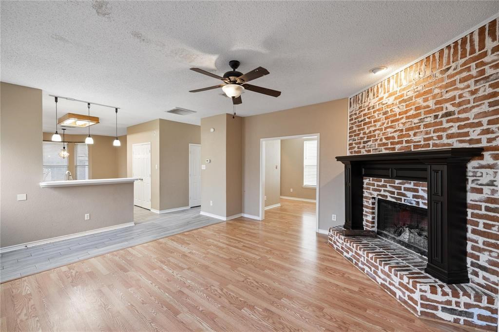 1414 Berkley Road Allen, TX 75002 - Photo 2 of 3 Living area featuring a floor-to-ceiling brick fireplace with a black mantel, wood-finish flooring, and a ceiling fan
