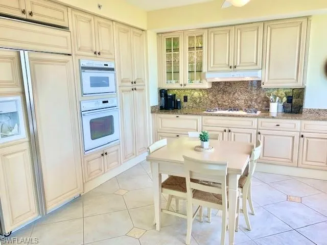 a white kitchen with granite countertop a stove a sink and a refrigerator