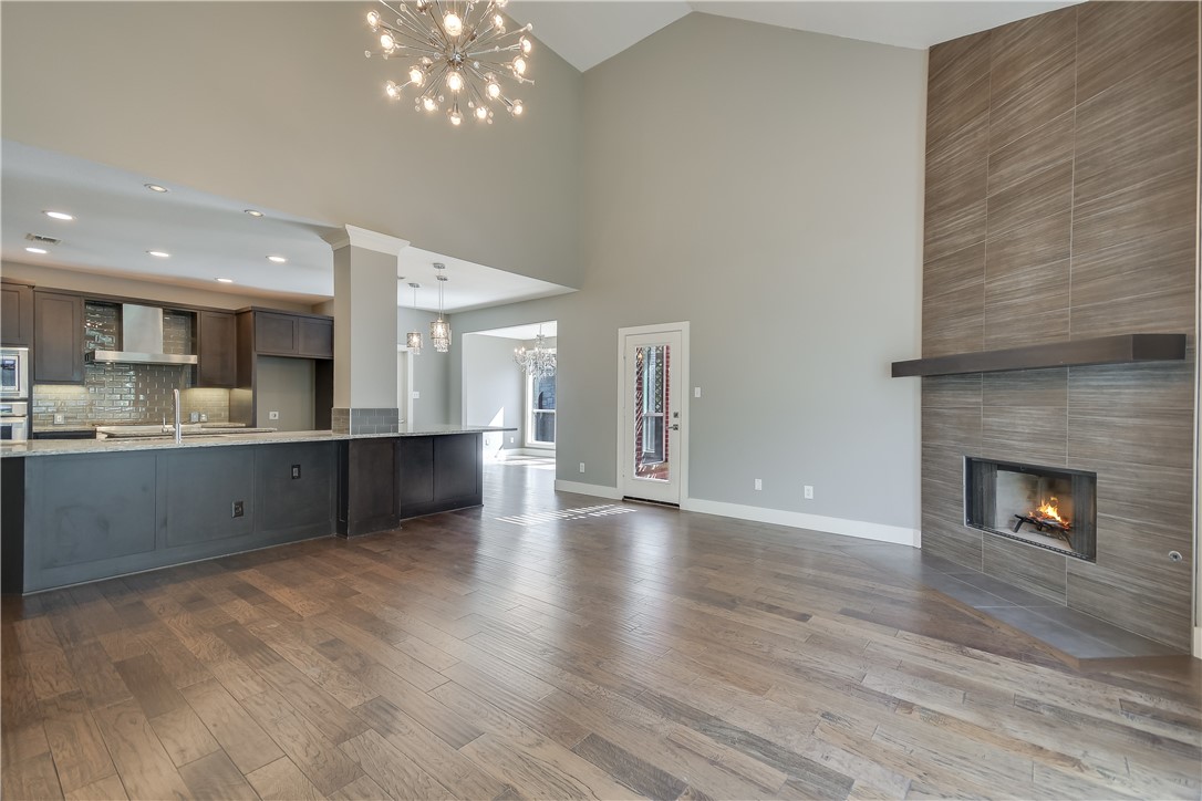 3513 Grimes Ranch Road Austin, TX 78732 - Photo 6 of 32 Unfurnished living room featuring a chandelier, high vaulted ceiling, a fireplace, wood finished floors, and baseboards