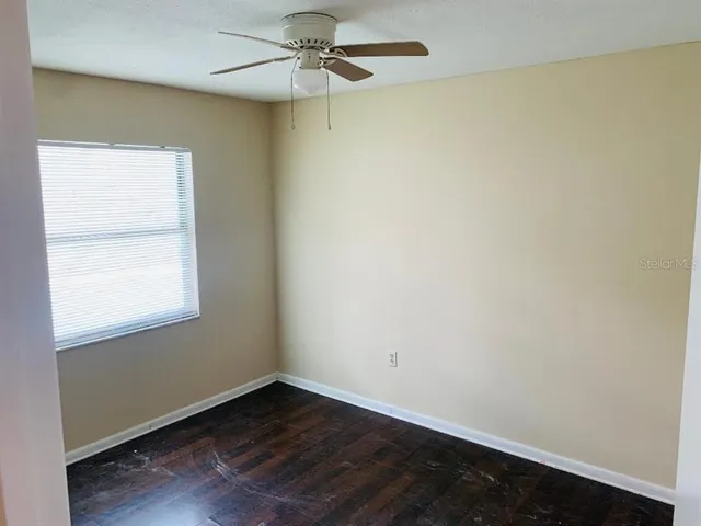 an empty room with wooden floor fan and windows