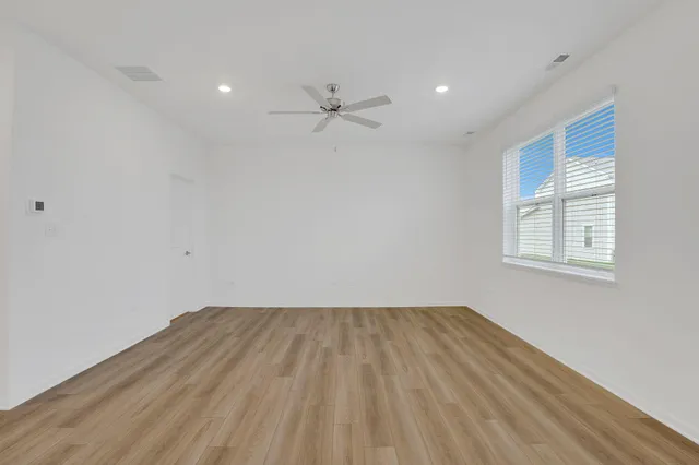 an empty room with wooden floor fan and windows