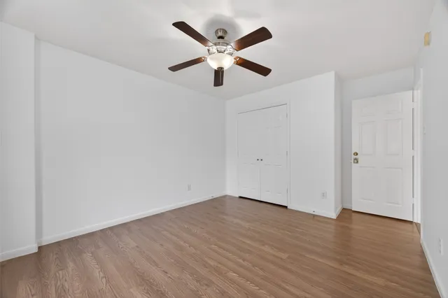 an empty room with wooden floor chandelier fan and windows
