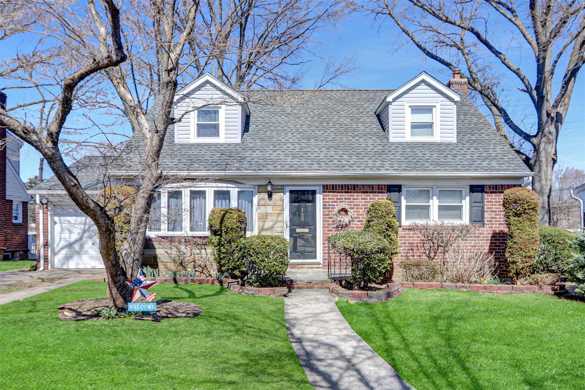 Cape cod home featuring a front lawn, a shingled roof, and brick siding