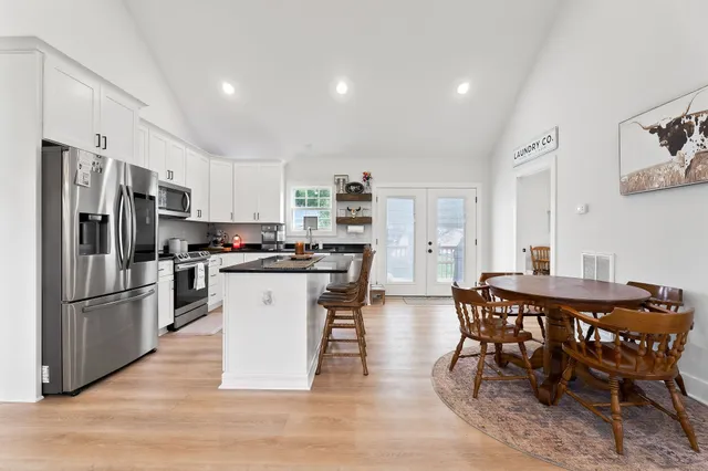 a kitchen with stainless steel appliances kitchen island granite countertop a dining table chairs and refrigerator