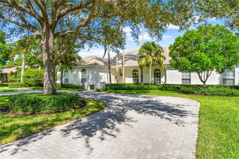 a view of a white house next to a yard with big trees