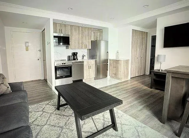 a living room with stainless steel appliances furniture a flat screen tv and kitchen view