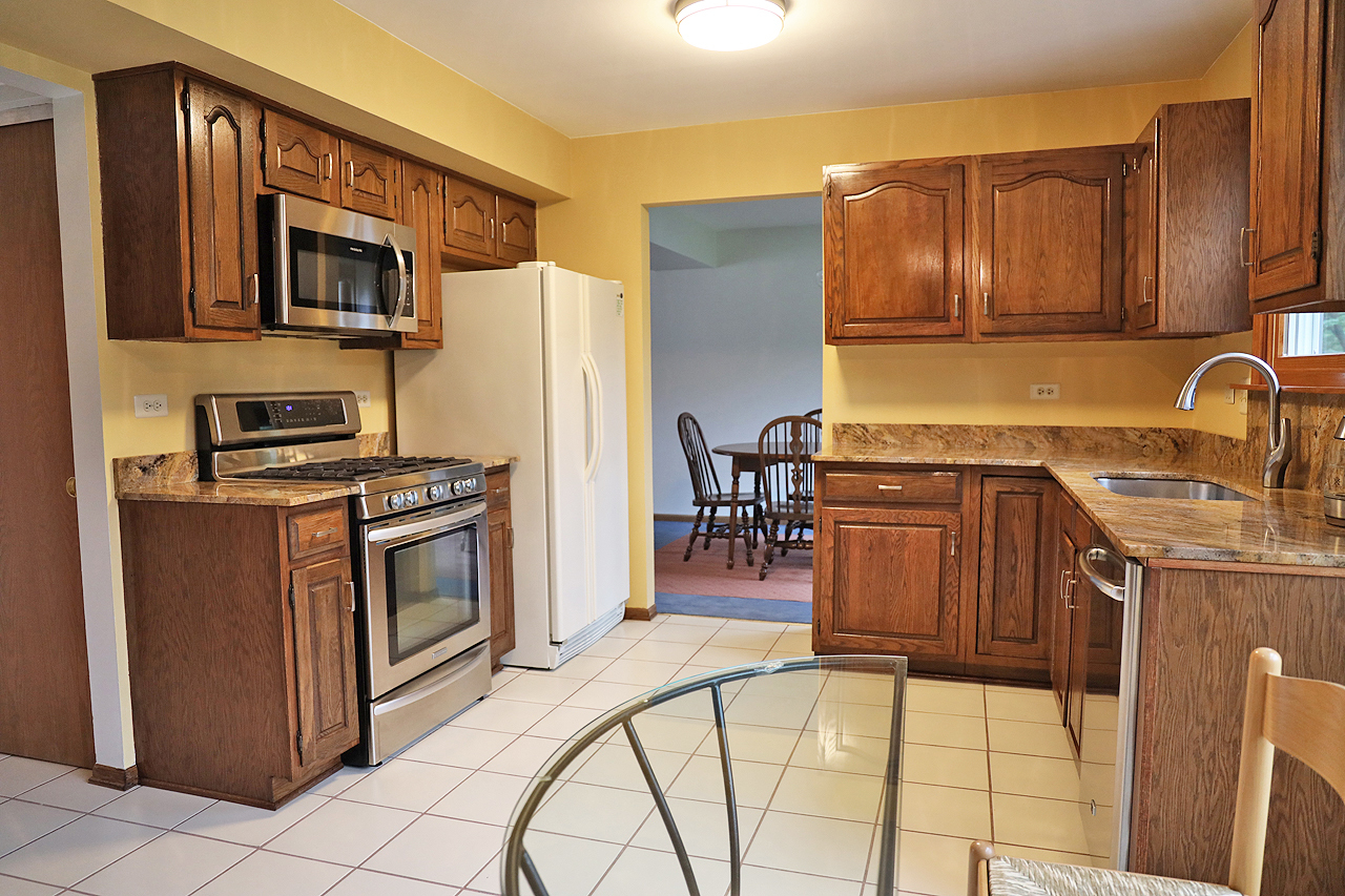 400 Barton Place Carol Stream, IL 60188 - Photo 20 of 45 a kitchen with stainless steel appliances granite countertop a stove a sink a refrigerator a dining table and chairs with wooden floor