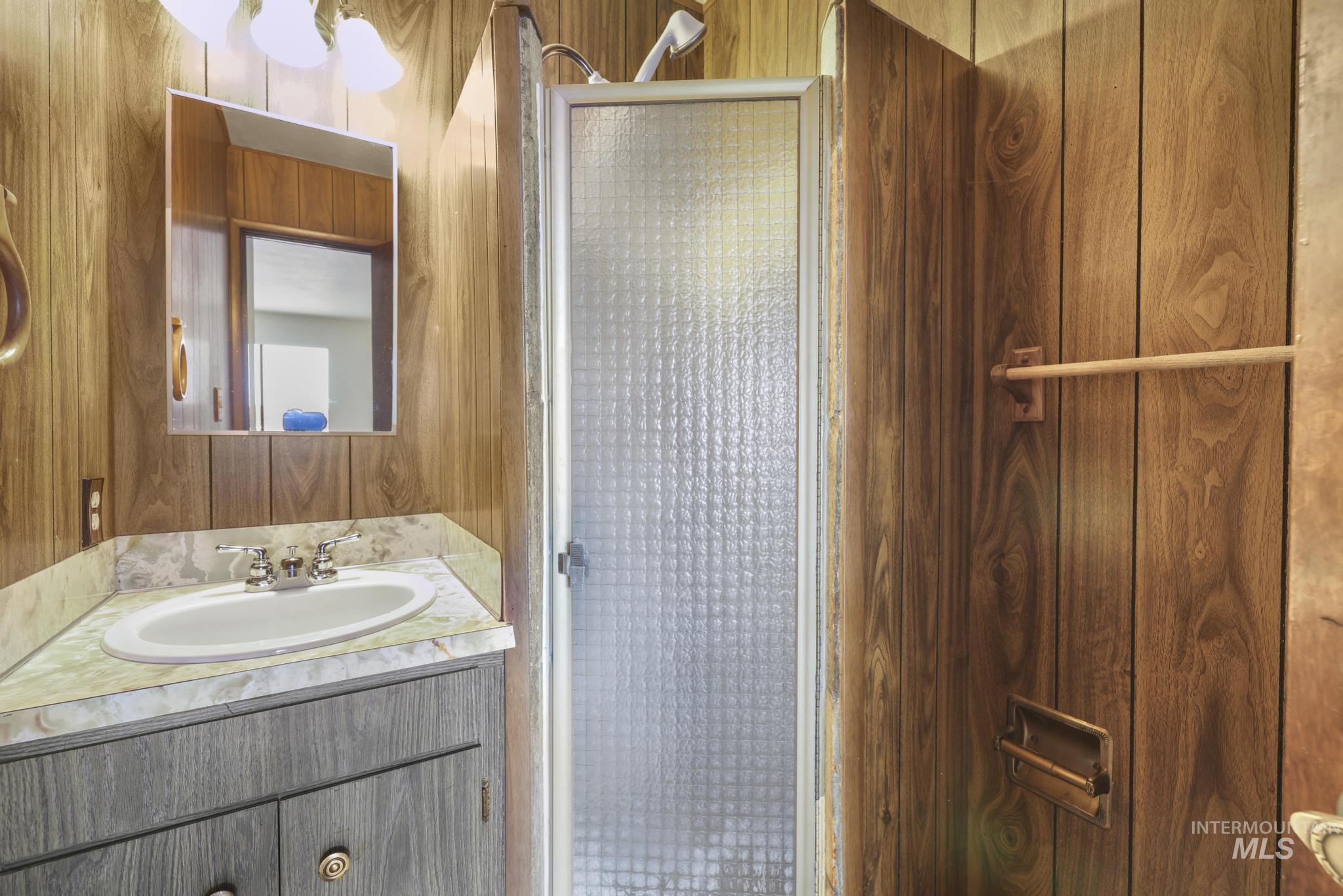 409 Clear Lakes Road Buhl, ID 83316 - Photo 16 of 43 Bathroom featuring wood walls, a stall shower, and vanity