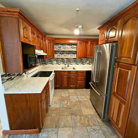 a kitchen with stainless steel appliances granite countertop a refrigerator a sink a stove top oven and cabinets